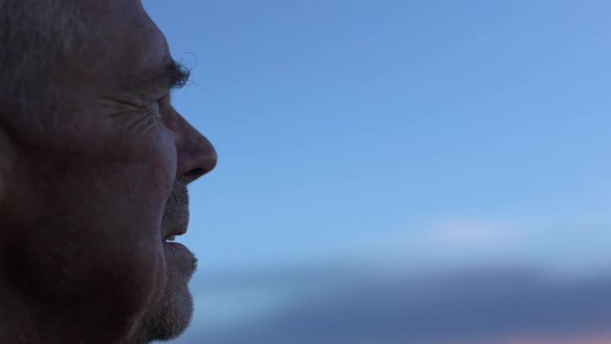 A man stands outside looking at the ocean and the sunset