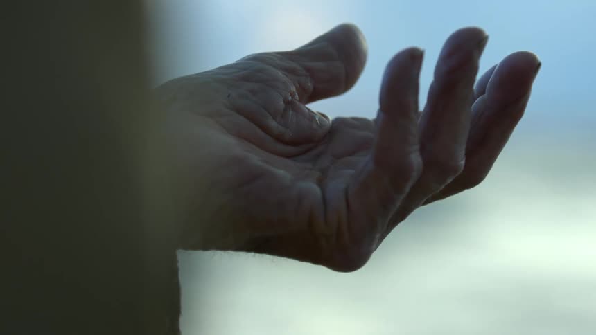 Palm of a hand with tear drops falling onto it at daytime next to a shoreline