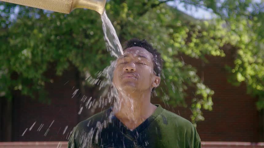 Boy standing outside in the day time under a golden vase pouring water on his face