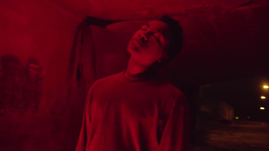 Young man standing under a concrete bridge closing his eyes while red lights strobe and flash around him