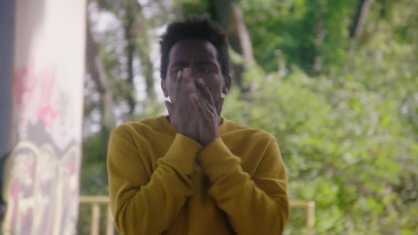 A black male looking nervous standing outside moving around and rubbing his hands together and touching his face