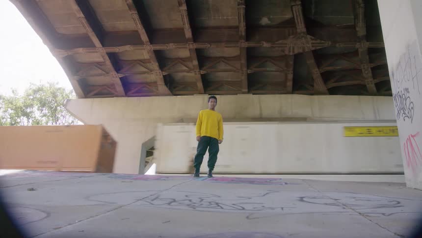 Boy standing on a slope in an underpass at daytime while a freight train passes behind him