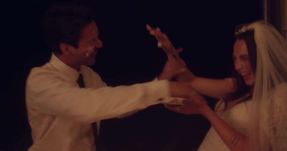 A newlywed couple laugh as they smash each other in the face with cake at their wedding