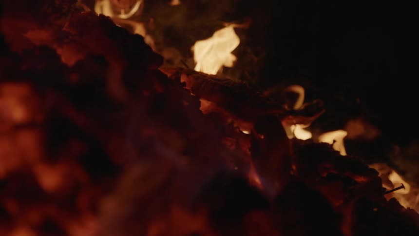 Close view of glowing embers of a fire in the dark that then reveals to a shot of the fires flames