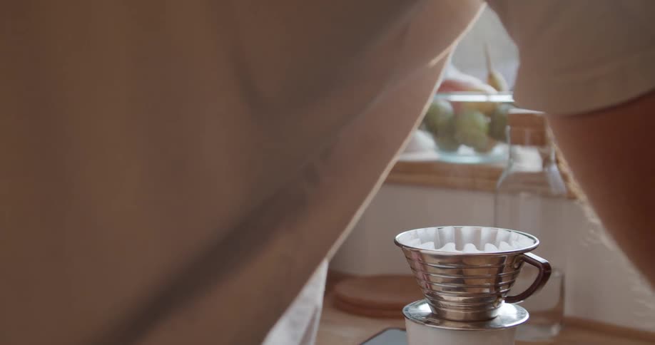 A man makes a pour over coffee in his kitchen and grabs his smartphone