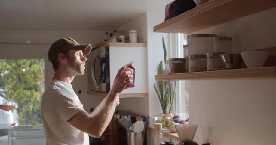 A man stands at the counter and reaches an item on a shelf in a kitchen