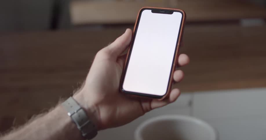 Man with a grey wristwatch uses a smartphone and holds a cup of coffee