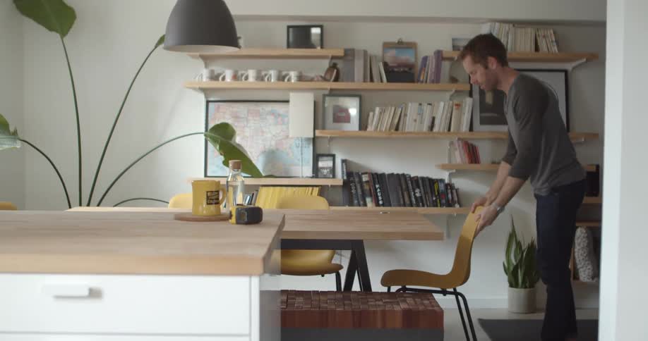 Man lifts a yellow chair off of a dining room tool picks up a measuring tape and walks out of the room