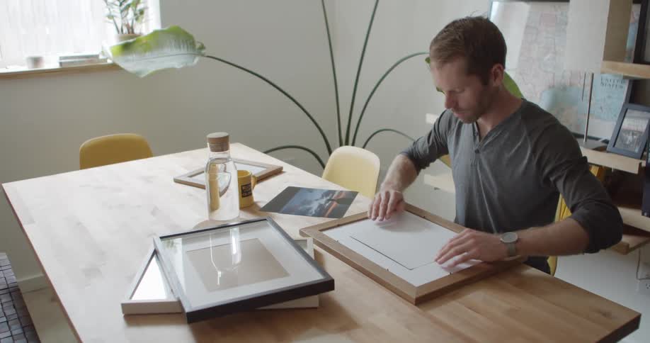 A man carefully aligns and places a photo into a picture frame