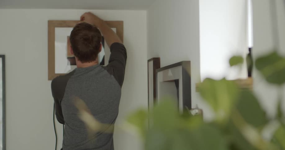 Man in his house hanging picture frames on white walls at daytime