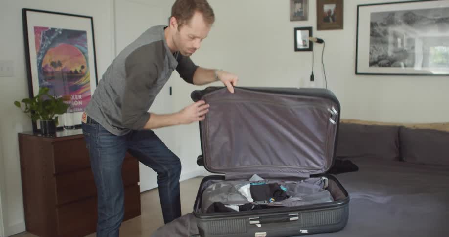 A man packs a suitcase and closes the top of it