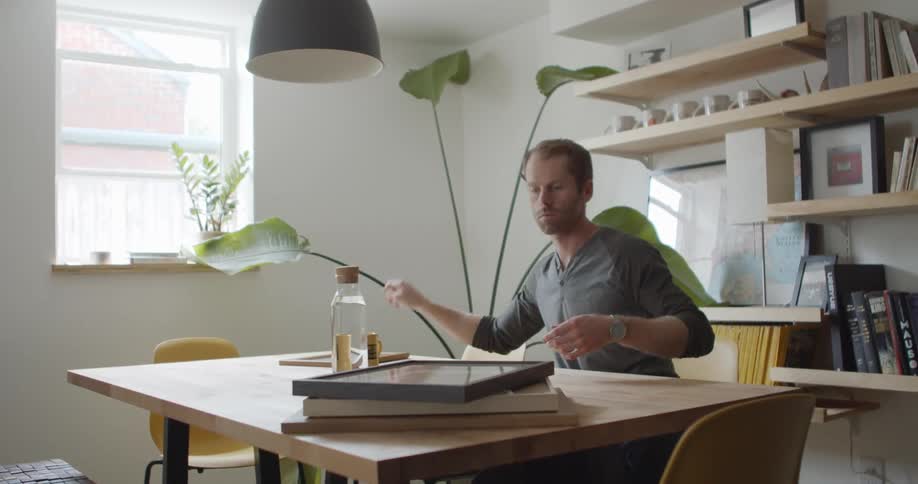A man sits at a table sorting through framed pictures