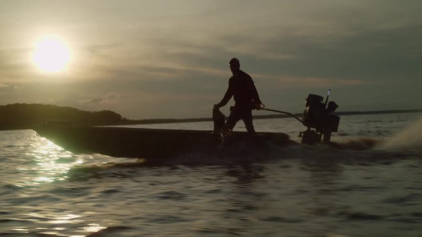 A man standing on a boat operating the motor