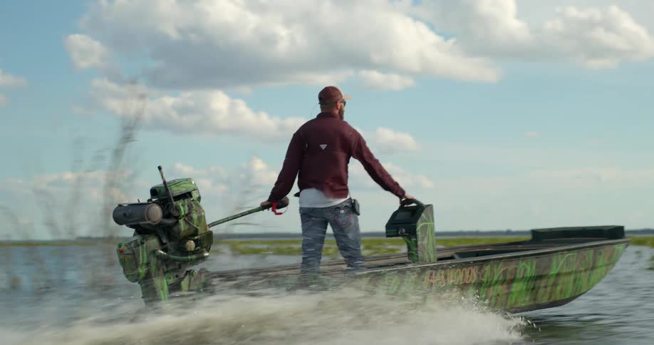 A man stands in a motorboat as he steers it through wetlands