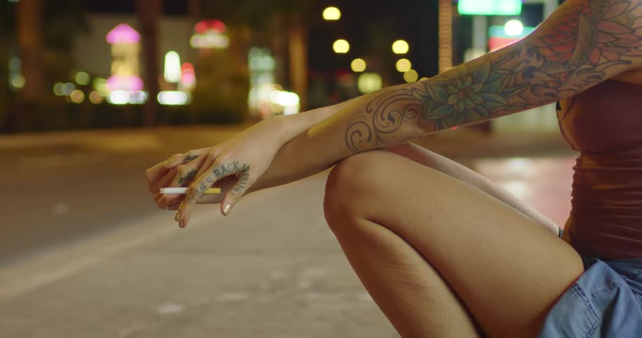 A woman sits on a city street smoking