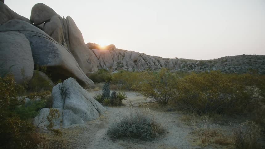 Empty desert plain with the sun setting over a hill of rocks