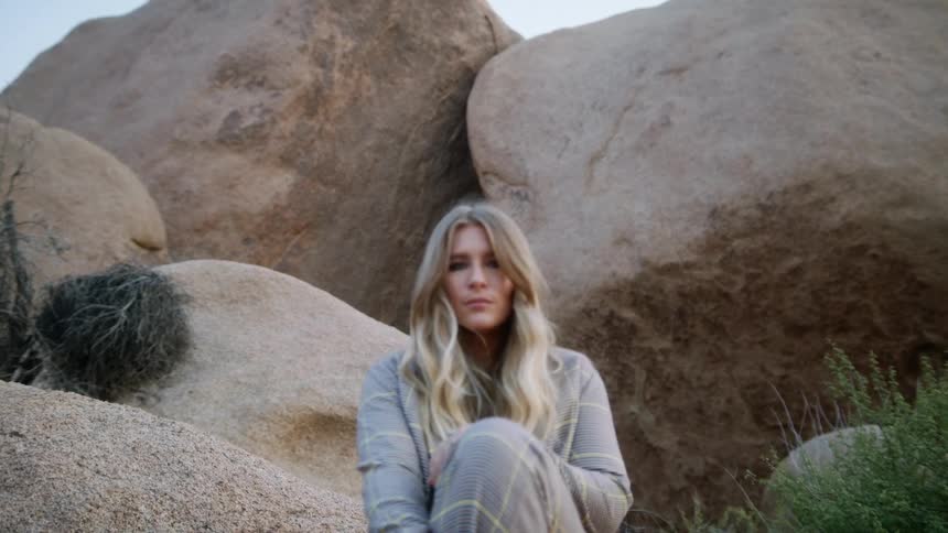 A young woman sits atop a boulder while posing for the camera