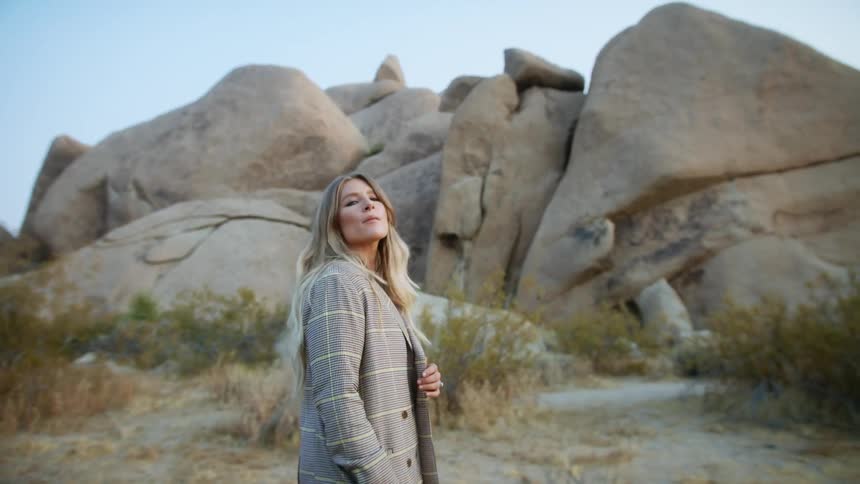 A woman in a plaid suit walks past a rock formation in the desert