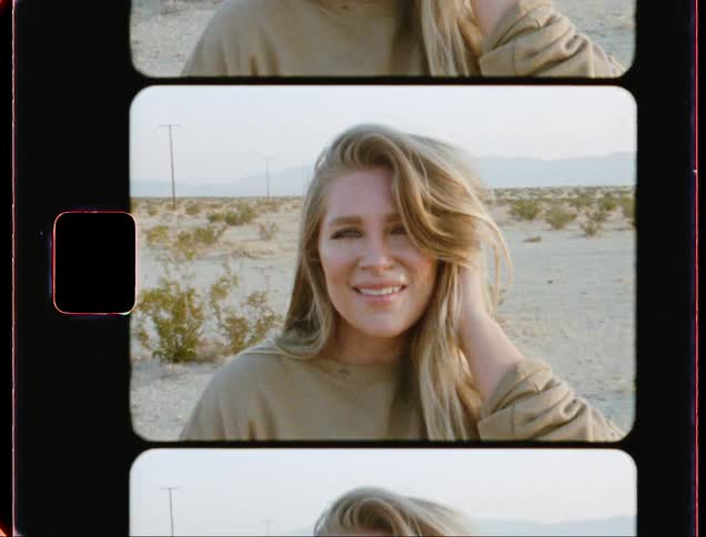 Blonde woman with a green sweater faces the camera with eye contact on the plain