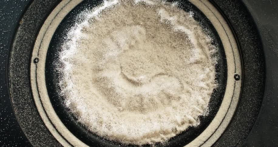 White granules are on a black speaker still and then moving with the vibrations