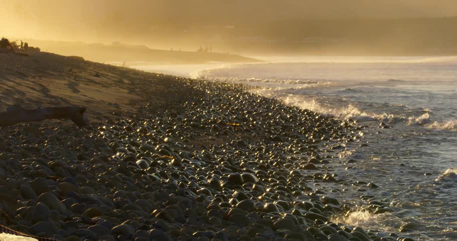 Small ocean waves wash upon a beach that is covered in smooth stones