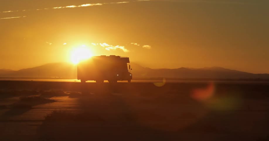 A large vehicle drives down the road at sunset