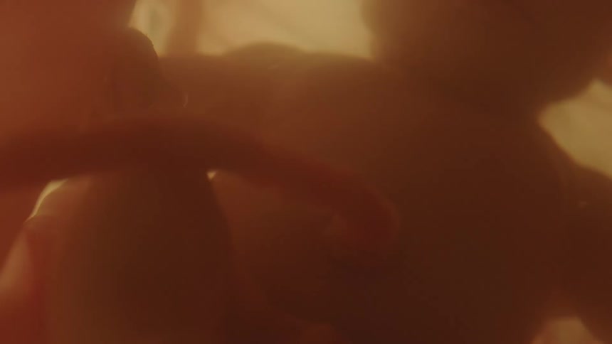 Unborn baby floating in gestational fluid is back lit by dim light