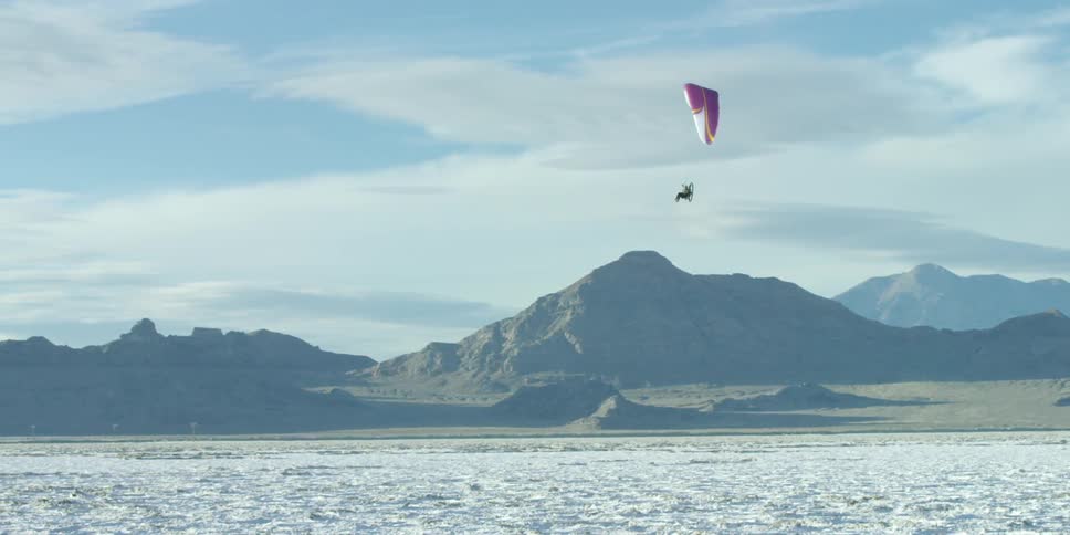 A paraglider sails across the sky above the flats and hills