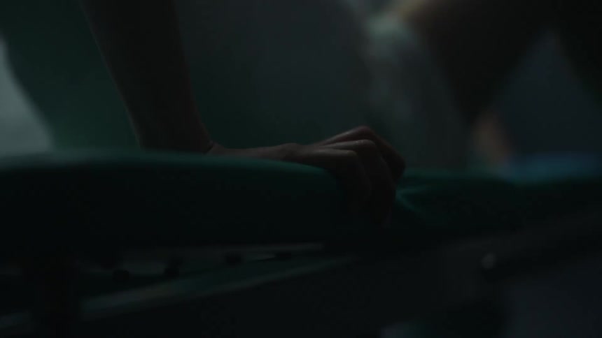 A hand grasps a blue mattress with a bare leg showing in a medical setting
