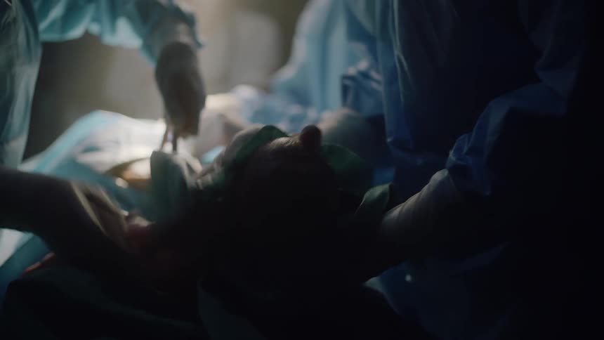 A doctor removes a newborn via cesarean section in an operating room and hands it to a staff member to clean
