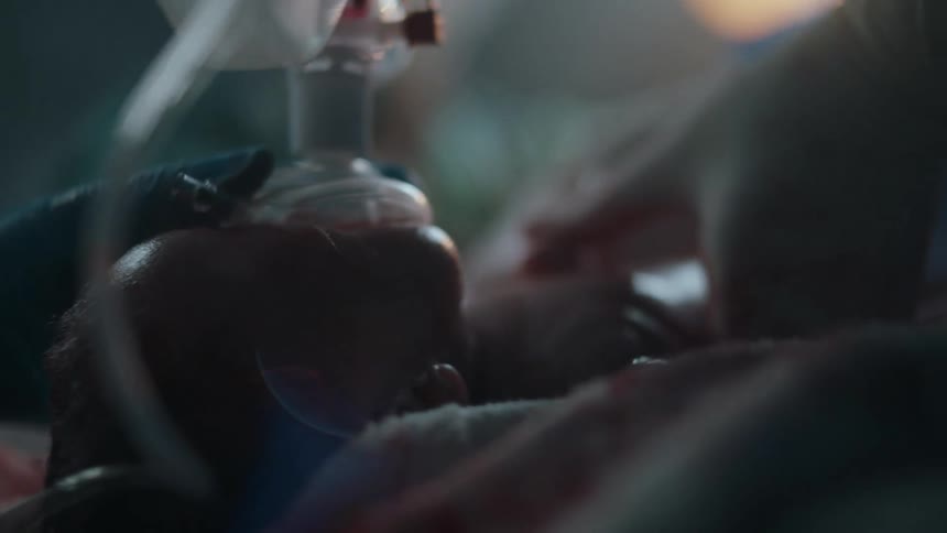 A newborn is given chest compressions by a medical person while oxygen is being given as well