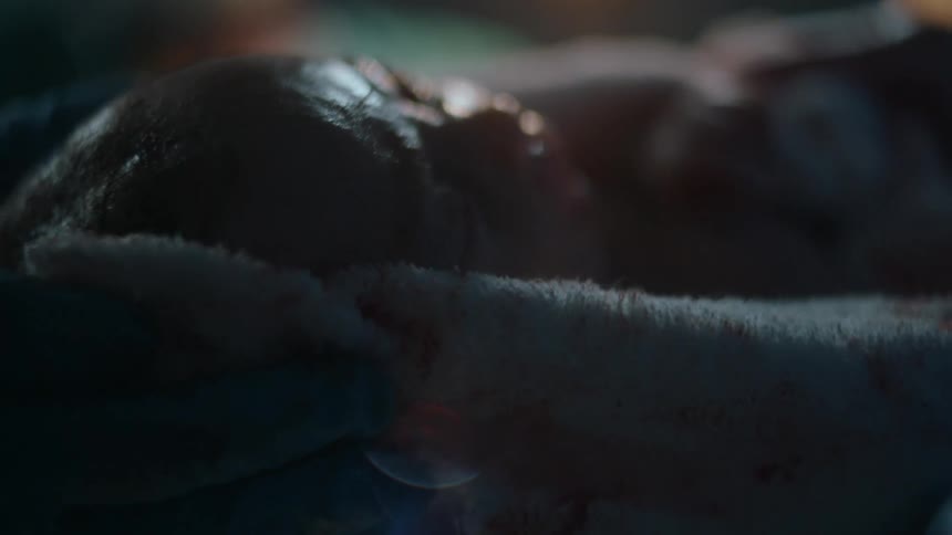 Newborn baby wrapped in towel is lifted by medical personnel in delivery room