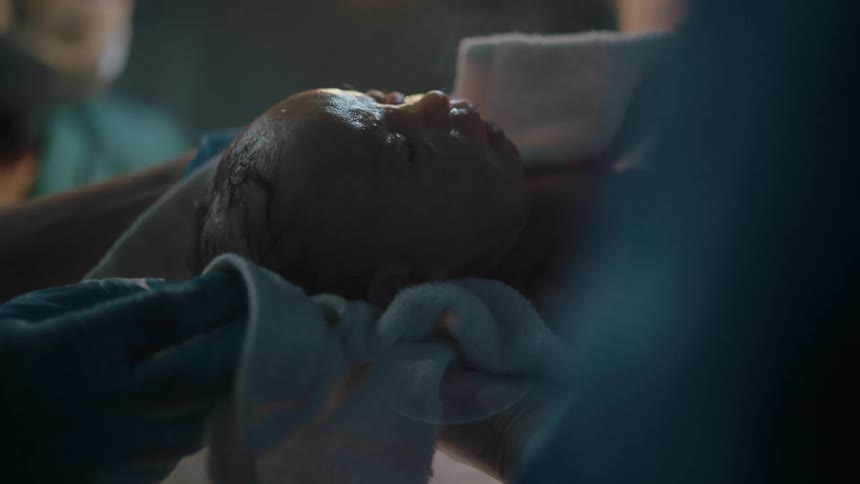 Doctors wearing personal protective equipment in a hospital operating room cradle a newborn baby in a blanket under surgical lighting