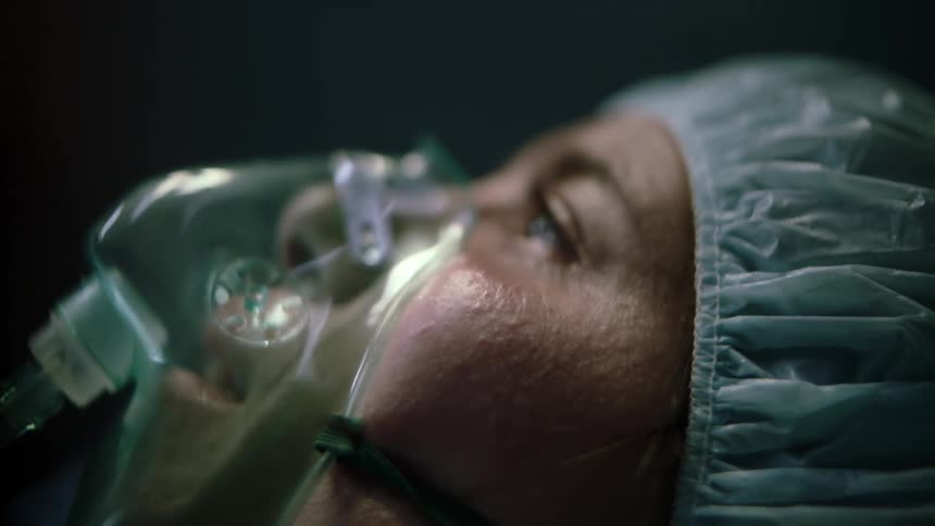 Woman lies on bed in operating theater breathing through breathing mask