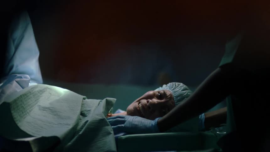A woman lies on a gurney in the operating room as a medical person comforts her and she smiles
