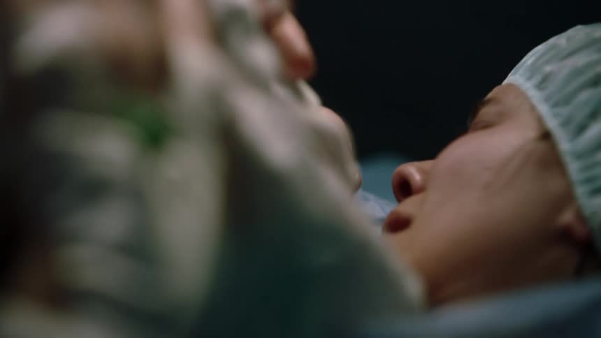 A just birthed baby is handed to the mother in an operating room by medical staff as she smiles in joy