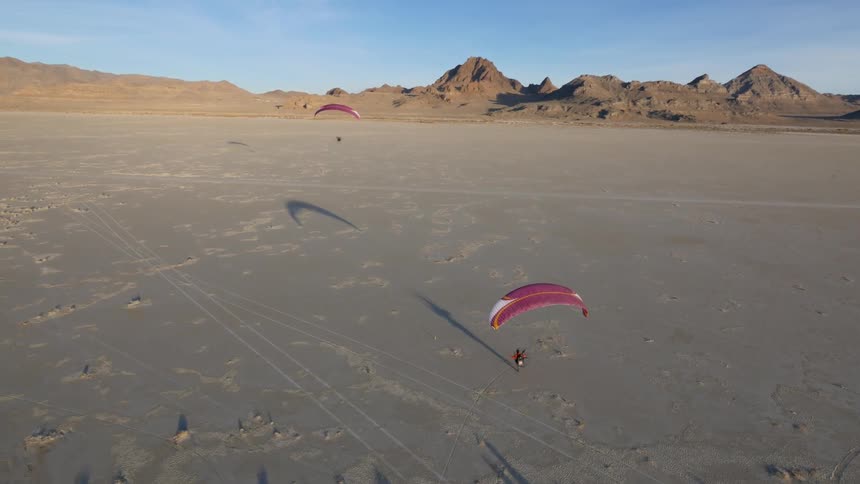 Two paragliders take off from a desert plain
