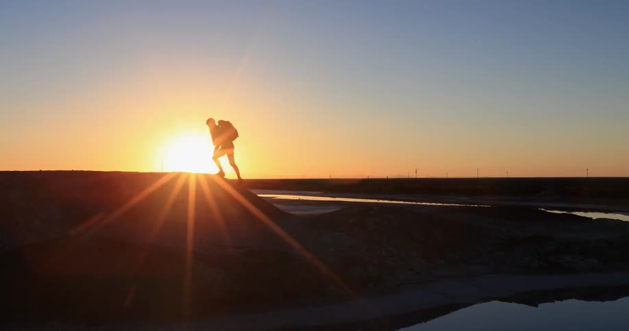 A woman wearing a backpack hikes at sunset