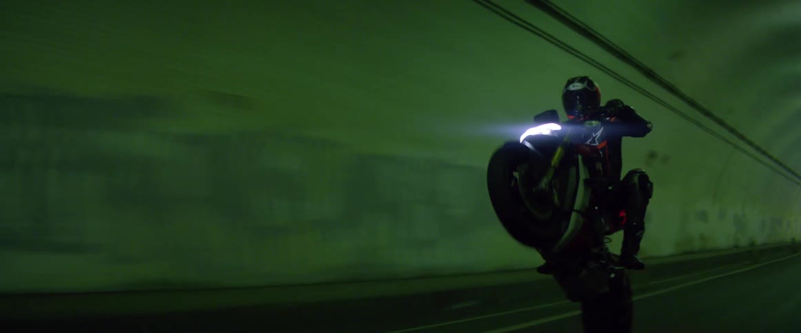 A person pulls up on their motorbike doing a wheely in a dark tunnel