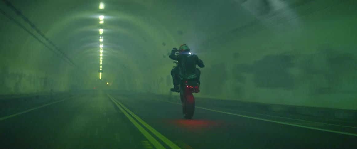 A person rides a motorcycle inside a tunnel doing stunts and wheelies