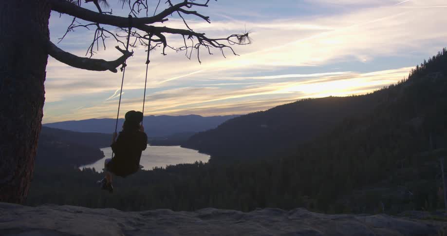 A woman swings on a makeshift swing hanging from a tree that overlooks a lake