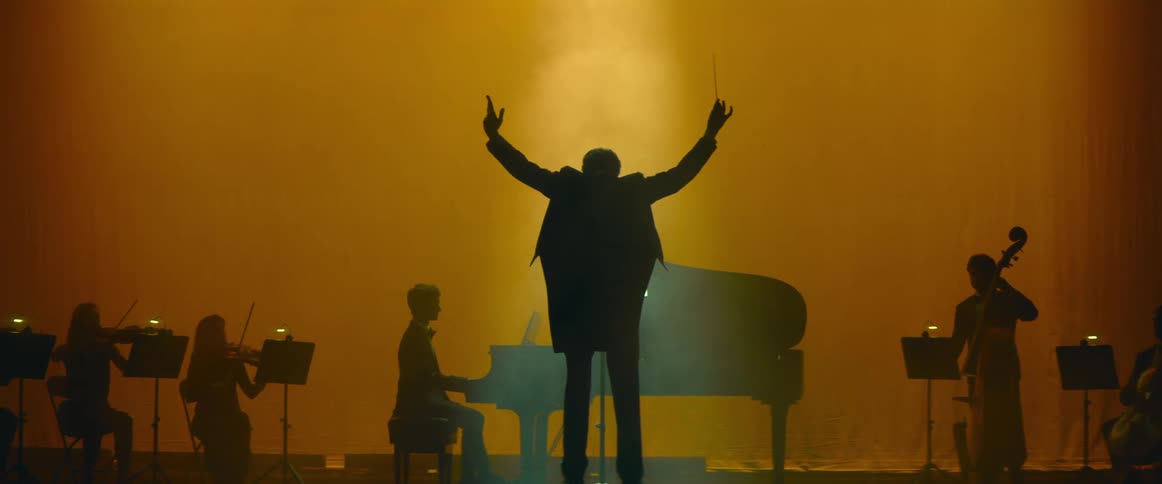 Silhouette of an orchestra on a stage and a conductor lifting his to ready them
