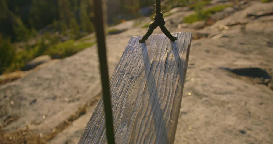 A wooden seat swing is empty as it overlooks a body of water and mountains