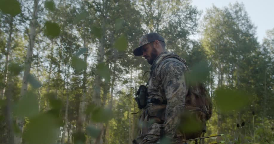 Man wearing military uniform holding a weapon walking in a forest next to skinny trees at day time