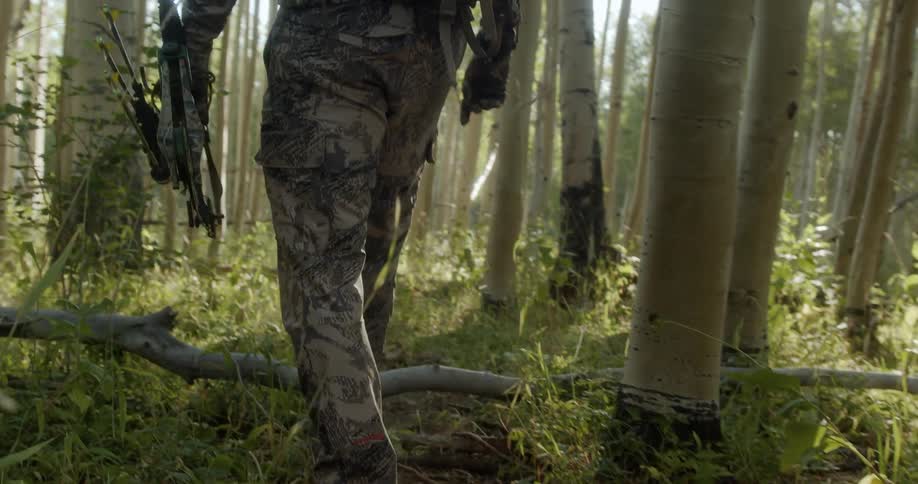 Man in camouflage walking through forest with compound bow on a hunt