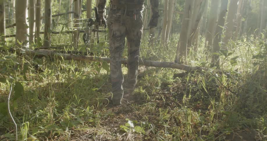 A male hunter walks through a forest wearing camouflage during the day