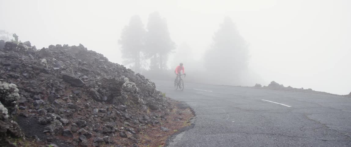 Cyclist riding uphill on a curved road through the mountains in the fog