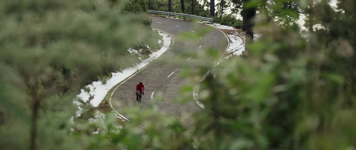 tele shot of a Cyclist pedaling up hill on a curvy forest road