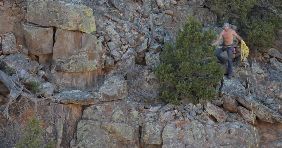 A man pulling up rope as he stands on the side of a cliff