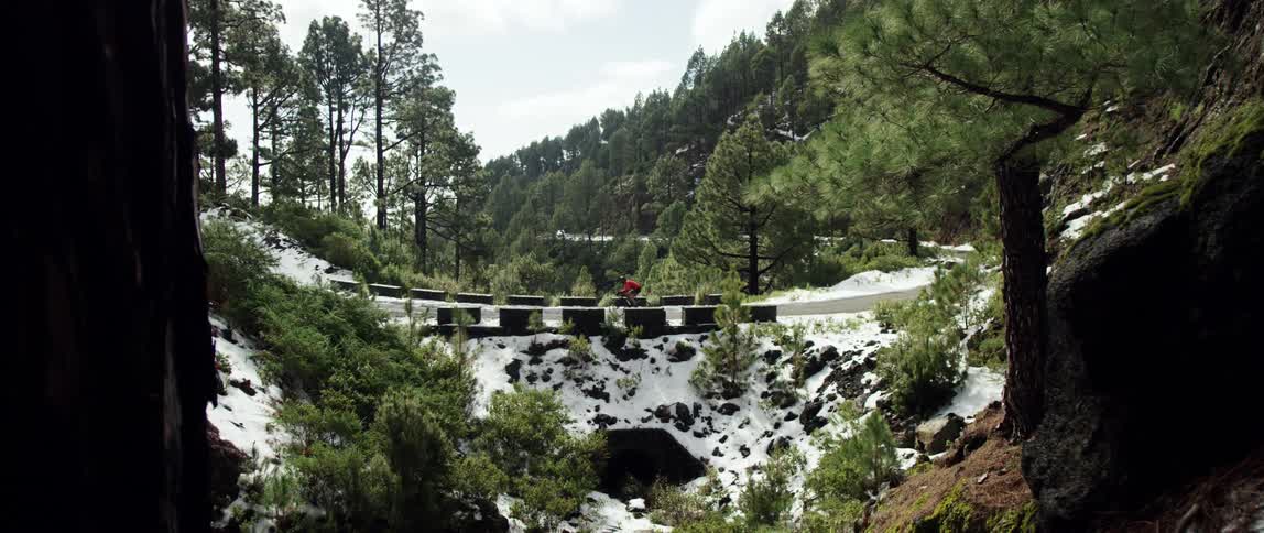 super wide shot of cyclist riding over a bridge on a paved road with hills covered in trees in the winter during the day